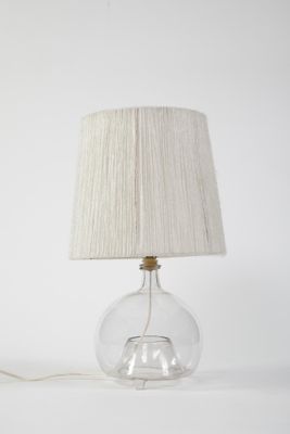 La lampe est en verre et est munie d'un abat-jour blanc.