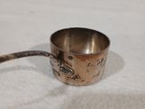 une petite tasse en argent posée sur une table, avec une cuillère à l'intérieur