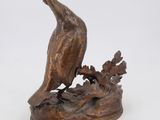 bronze sculpture of a bird perched on a branch with leaves