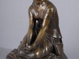 statue en bronze représentant une femme assise par terre, les mains posées sur les genoux