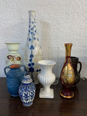 de nombreux vases de styles variés posés sur une table, avec un mur blanc en arrière-plan