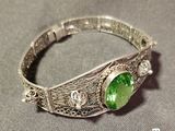 silver bracelet with a green stone in the middle of it on a gray surface