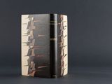 an old book with a black cover sitting on top of a table