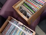 deux boîtes remplies de CD posées sur une chaise violette