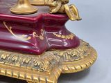 a red and gold clock on a stand with a cup on it