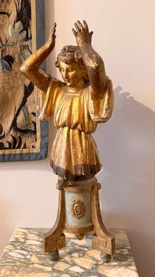 une statue d'enfant posée sur un socle devant un tableau