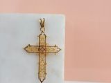 pendentif en forme de croix en or jaune posé sur un bloc de marbre blanc, sur fond rose