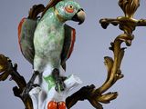 a figurine of a parrot sitting on a branch with a candelab