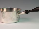 a silver sauce pot with a wooden handle on a white table