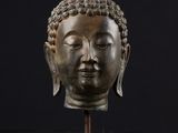 une tête de Bouddha en bronze posée sur un socle en bois