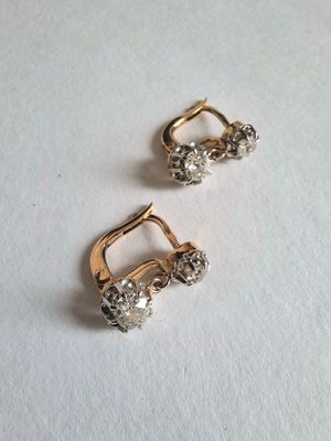deux paires de boucles d'oreilles en or et diamants posées sur une surface blanche
