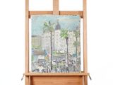 un tableau posé sur un chevalet, avec en arrière-plan un tableau représentant un paysage urbain