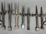 six vieux outils en fer sont alignés sur une surface blanche