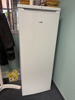a white refrigerator in the corner of a room with a coat rack