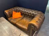 a brown leather couch with an orange pillow on top of it
