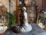a bronze statue of a boy sitting on a rock