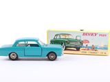 une petite voiture devant une boîte de jouets Dinky Toys posée sur une surface blanche