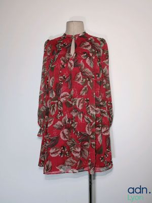 une robe à fleurs rouges posée sur un mannequin contre un mur blanc