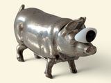 a small metal pig with big eyes on a white surface