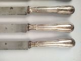 four silverware knives are lined up on a white surface