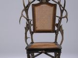 une image représentant une chaise dont le dossier est orné de bois de cerf et dont l'assise est en osier