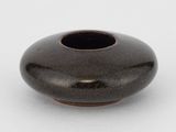 un petit vase noir posé sur une surface blanche