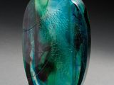 un vase en verre vert et bleu posé sur une surface blanche