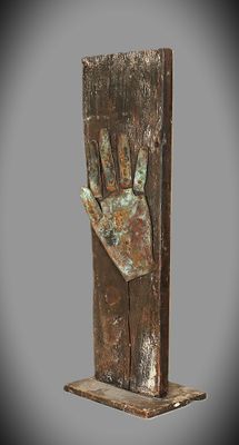 sculpture en bronze représentant une main tenant un morceau de bois, posée sur un socle