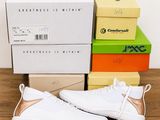 des baskets blanches et dorées posées sur une table en bois, à côté de piles de cartons
