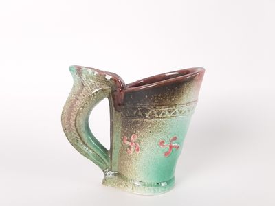 une tasse verte et marron avec une anse, posée sur un fond blanc