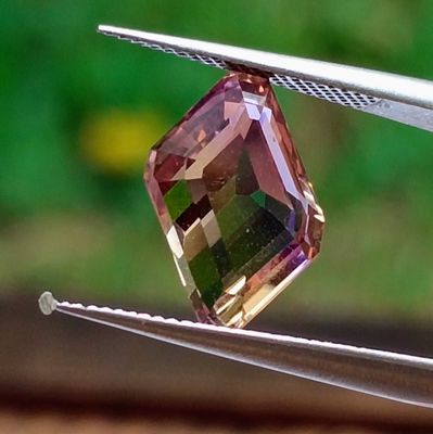 a pink and green diamond being held by a pair of pliers