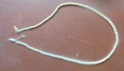un collier de perles blanches muni d'un fermoir en argent, posé sur une table