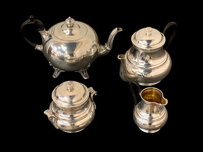 trois théières en argent et une tasse posées sur une table