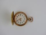 une montre de poche en or sur une surface blanche
