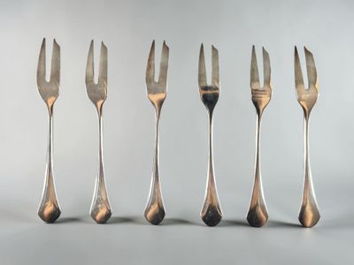 six forks are lined up in a row on a white surface