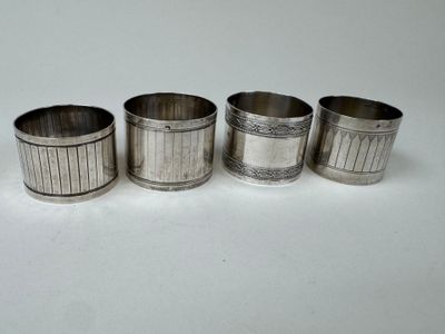 four silver napkin rings with designs on them on a white surface