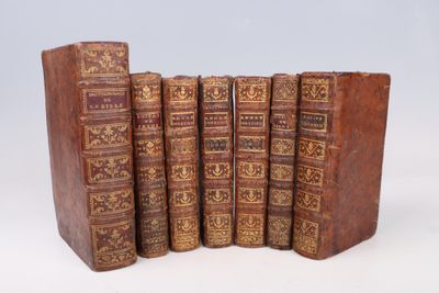 six old books are lined up in a row on a white surface