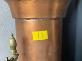 a large copper pot sitting on a shelf next to a wall