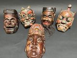 five wooden masks with different faces are sitting on a table
