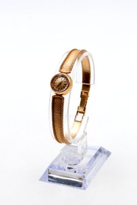 une montre en or posée sur un socle transparent, sur un fond blanc