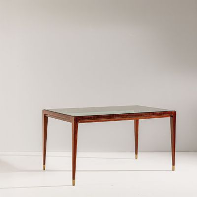 une table avec un plateau en verre et des pieds en laiton dans une pièce blanche