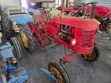 a red tractor parked in a garage with other old tractors