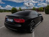 a black car parked in a parking lot with clouds in the background