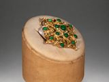 an image of a gold ring with green stones on top of a wooden box