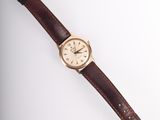 a close up of a watch on a white surface with a brown strap