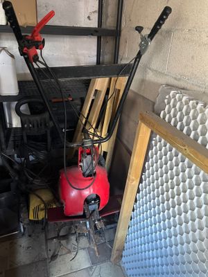 a red snow blower sitting in a garage next to a pile of tools