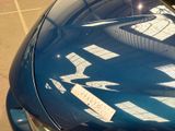 a blue car parked in a parking lot with a sticker on it ' s hood