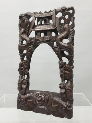 un vieux cadre en bois orné de sculptures, exposé dans une vitrine transparente