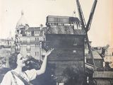 an old picture of a woman standing on a roof with a windmill in the background