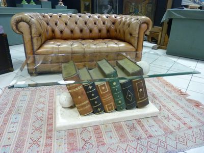 a glass table with books on it and a leather couch in the background